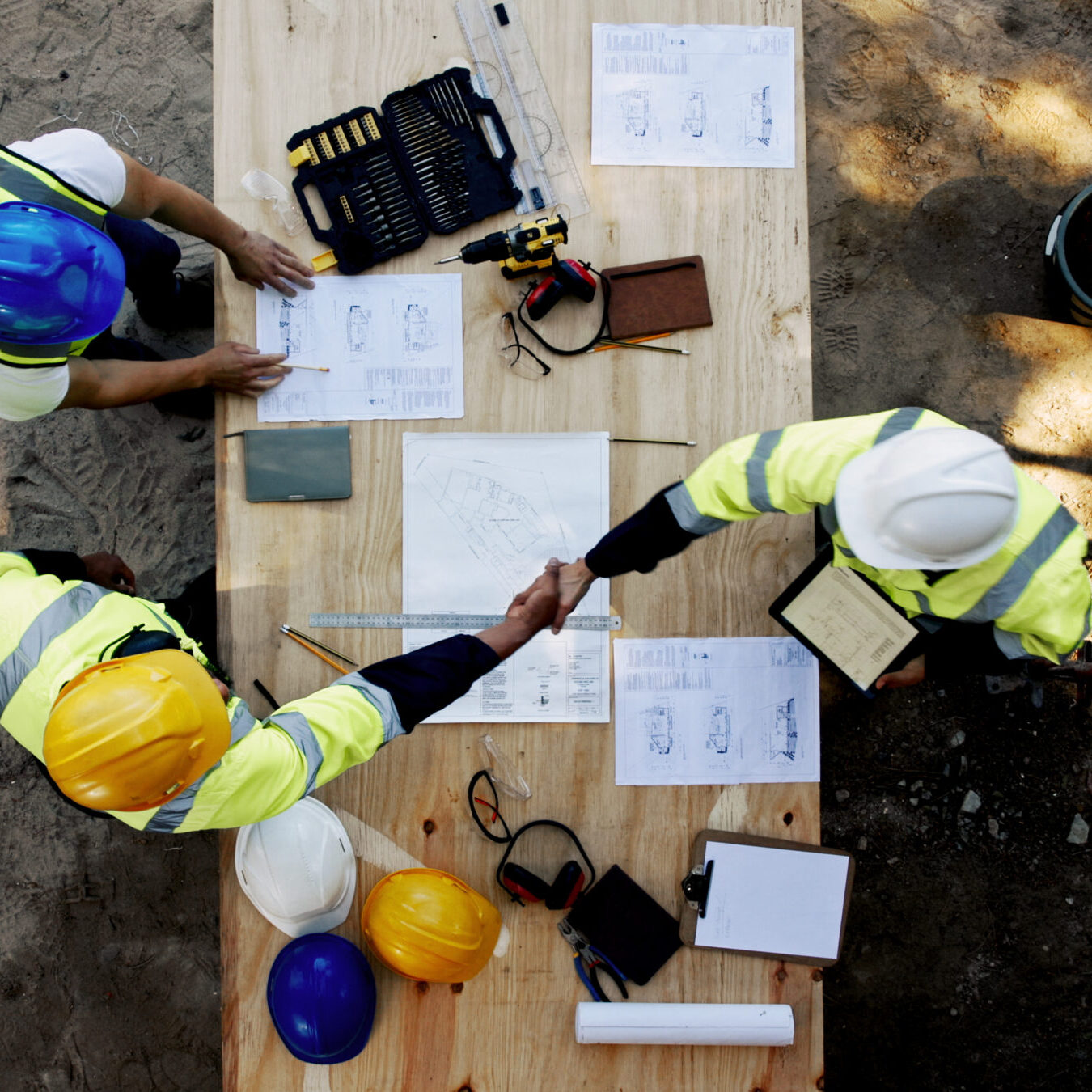 Blueprint, architecture and men at table shaking hands for collaboration, agreement and inspection from above. Construction, building team and contractor on site with floor plan, handshake and deal Blueprint, architecture and men at table shaking hands for collaboration, agreement and inspection from above. Construction, building team and contractor on site with floor plan, handshake and deal